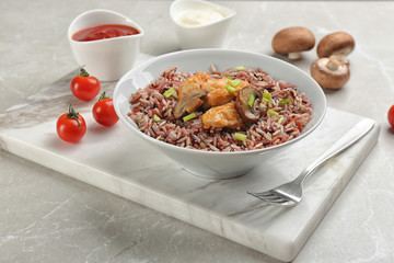 Tasty brown rice with chicken and mushrooms on light grey marble table