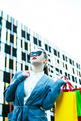 young pretty girl with colorful bags posing in sunglasses outside in city, lifestyle people concept