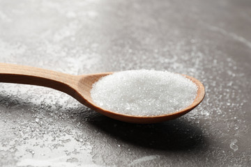 Spoon of white sugar on marble table, closeup