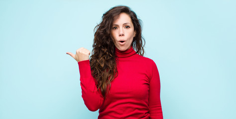 young pretty woman looking astonished in disbelief, pointing at object on the side and saying wow,...