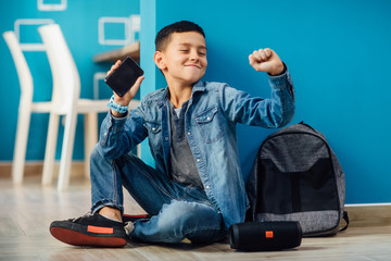 A small boy in the room with a phone in his hands connects a music column on bluetooth.