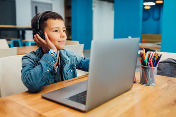 Child concentrated boy with laptop doing homework.