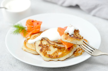 Fritters with salted salmon and sour cream.  A fork with a piece of pancake in the frame.  Light background.  Close-up.