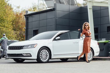 Confident businesswoman informal dress outdoors posing near her white car.