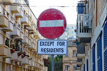 Red and white circular no entry sign except for residents in front of a block of apartments.