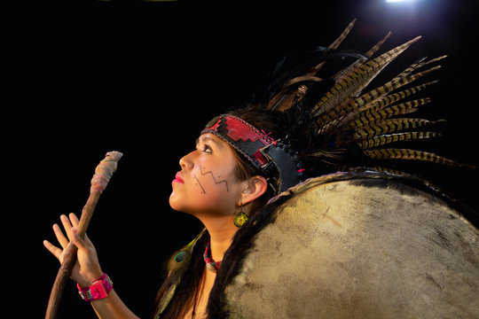 close up of young woman Teotihuacana, Xicalanca - Toltec in black background, with traditional dress dance with a trappings with feathers and drum
