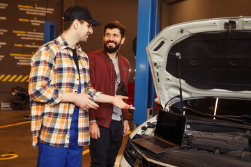 Fototapeta na wymiar workman and customer talking about repairing car using laptop in the garage