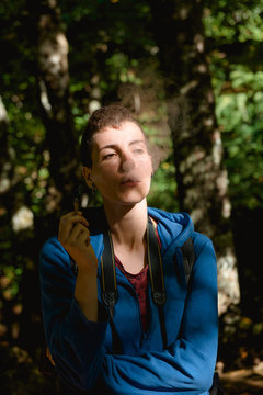 Calm young female tourist resting and smoking marijuana joint while hiking in forest in summer