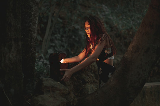 From below of young female in dress taking ancient retro clock in wooden box on stone in autumnal forest