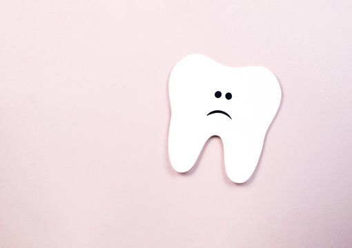 white paper tooth with sad eyes and mouth on a pink background