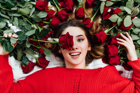 Happy Woman Covering Eye With Rose Flower Lying On The Bed With Roses, Overhead Shot