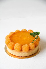 French dessert tart with coconut, mango, passion fruit, yellow raspberries and mint, and also Italian meringue as decoration. Tart is on a golden cardboard cake base, on a white background.
