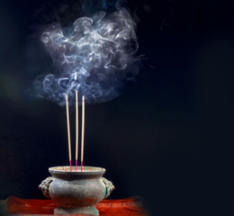 Holder and burning incense sticks with a lot of smoke on dark background