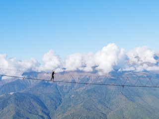A girl in a helmet crosses a suspension bridge over a mountain gorge on a clear day