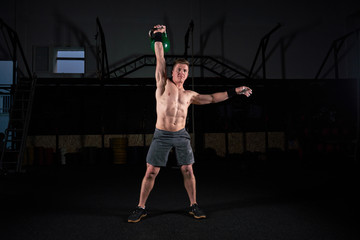Strong man with dumbbell in his hand doing strength exercises in the gym with magnesium in his hands. Young athlete practicing multidisciplinary training