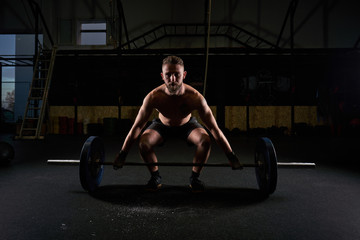 Strong man with barbell with weights in his hands doing strength exercises in the gym with magnesium in his hands. Young athlete practicing multidisciplinary training