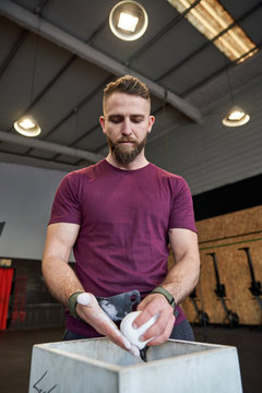 Strong man prepares to exercise in the gym with magnesium in his hands. Young athlete practicing multidisciplinary training