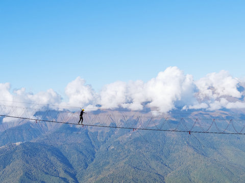 Fototapeta A girl in a helmet crosses a suspension bridge over a mountain gorge on a clear day