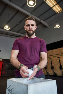Strong man prepares to exercise in the gym with magnesium in his hands. Young athlete practicing multidisciplinary training