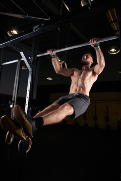 Strong man doing strength exercises on a bar in the gym with magnesium in his hands. Young athlete practicing multidisciplinary training