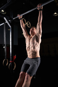 Strong man doing strength exercises on a bar in the gym with magnesium in his hands. Young athlete practicing multidisciplinary training