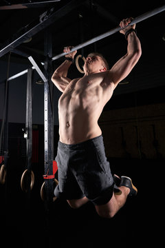 Strong man doing strength exercises on a bar in the gym with magnesium in his hands. Young athlete practicing multidisciplinary training