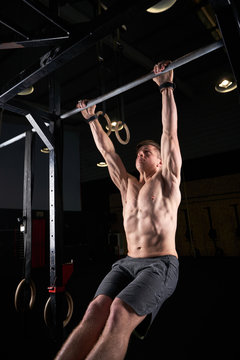 Strong man doing strength exercises on a bar in the gym with magnesium in his hands. Young athlete practicing multidisciplinary training