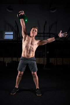 Strong man with dumbbell in his hand doing strength exercises in the gym with magnesium in his hands. Young athlete practicing multidisciplinary training