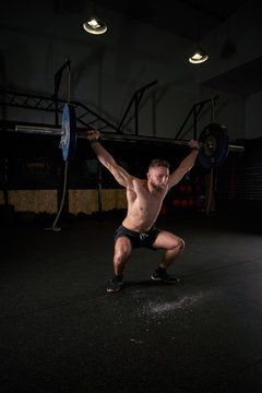 Strong man with barbell with weights in his hands doing strength exercises in the gym with magnesium in his hands. Young athlete practicing multidisciplinary training