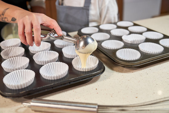Stock photo of a hand of a girl emptying cream with the ice cream scoops in plates prepared with pastry paper for cupcakes