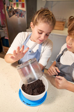 Stock vertical photo of a girl wearing an apron pouring the content of a container into a bowl