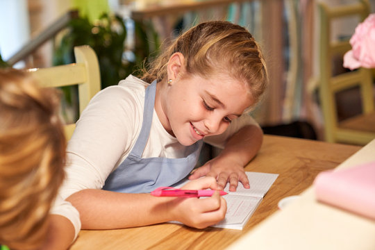 Stock photo of a girl sitting in front of a wooden table writing in a notebook and with a notebook and flowers in front of her - Powered by Adobe