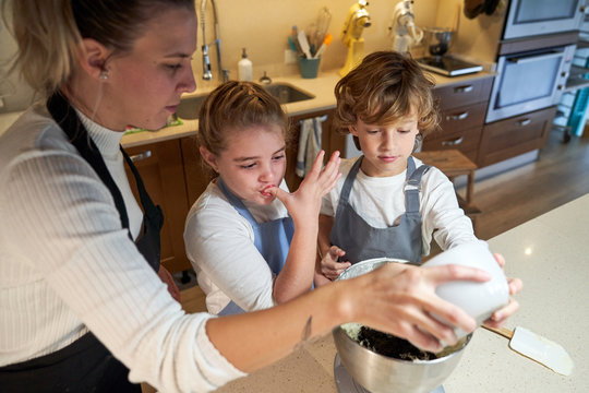 Stock photo of two boys and a girl with apron in the kitchen mixing ingredients preparing cupcakes