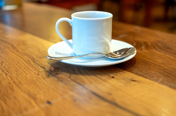 Weiße Kaffeetasse mit Untertasse und Löffel auf einem rustikalen Holztisch – selektiver Fokus mit viel Tiefenunschärfe und Copyspace