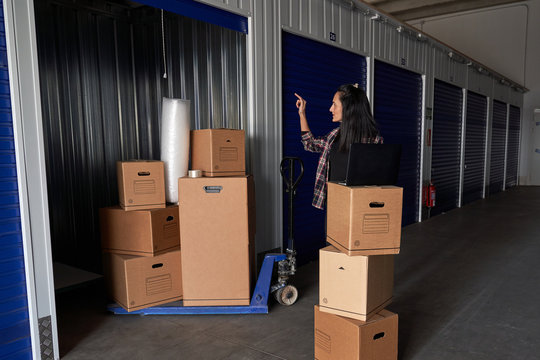 Woman working with a laptop in a moving storage room organizing the boxes in a self storage warehouse