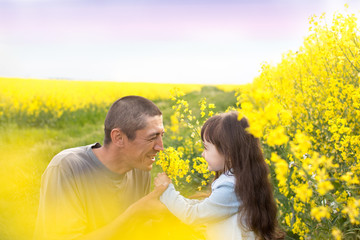 a little girl with her father in a field of flowering yellow rapeseed. rapeseed field. father holding daughter's hands