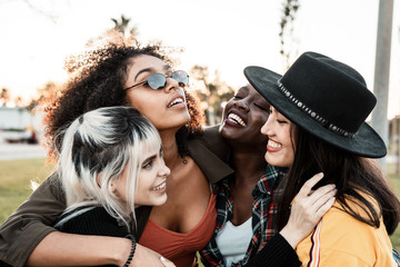 Group portrait of diverse young women wearing clothes in hipster style looking at each other with smiles and hugging together  