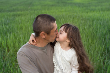 a little girl with long hair with her father in a field of green wheat. young wheat. father and daughter