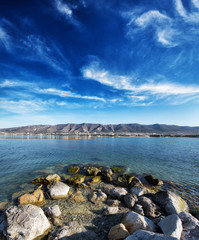 Fototapeta na wymiar Autumn panorama of Gelendzhik Bay. Clear air, clear sky, and sharp clarity. In the foreground are rocks and a beach. In the background the Caucasus mountains