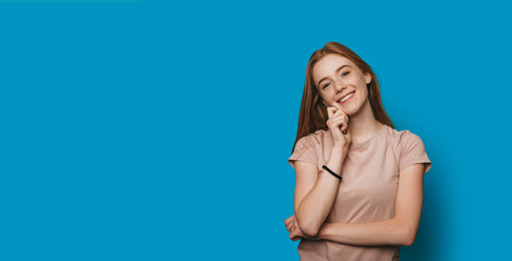 Portrait of a lovely young woman with red hair with freckles looking at camera laughing touching...