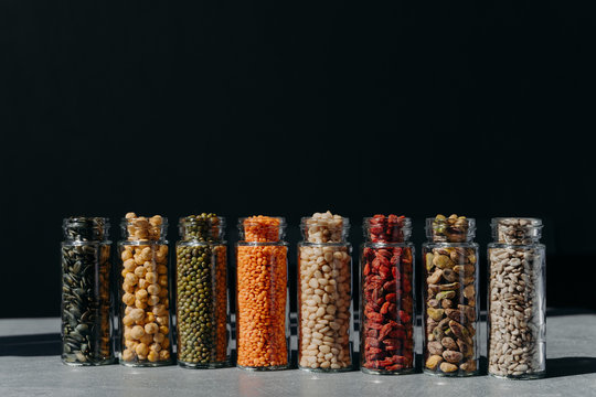Healthy products in glass containers for good safe storage. Se of pimpkin seeds, chickpea, various beans, nuts and berries in bottles on dark background