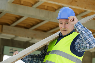 worker at carpentry shop smiling and carrying wood