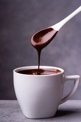 in the foreground, hot and liquid chocolate pouring from the spoon into a white ceramic cup