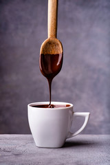 in the foreground, hot and liquid chocolate pouring from the spoon into a white ceramic cup