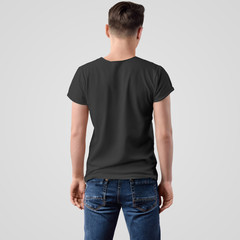 Obraz premium Mockup of a black T-shirt on a young guy in blue jeans, standing back, on a white background.