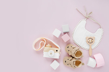 Cute shoes, bib and wooden toys. Set of baby stuff and accessories for girl on pastel pink background.  Baby shower concept.  Fashion newborn. Flat lay, top view