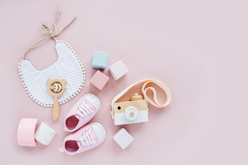 Cute shoes, bib and wooden toys. Set of baby stuff and accessories for girl on pastel pink background.  Baby shower concept.  Fashion newborn. Flat lay, top view