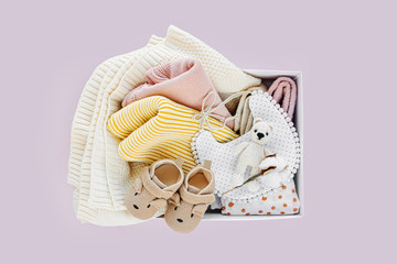Box with baby stuff and accessories for newborn on pastel pink background. Knitted blanket,...