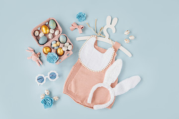 Cute baby costume Easter bunny. Knitted bodysuit with fluffy  bunny ears, Easter eggs and candy on blue background. Holiday concept. Flat lay, top view