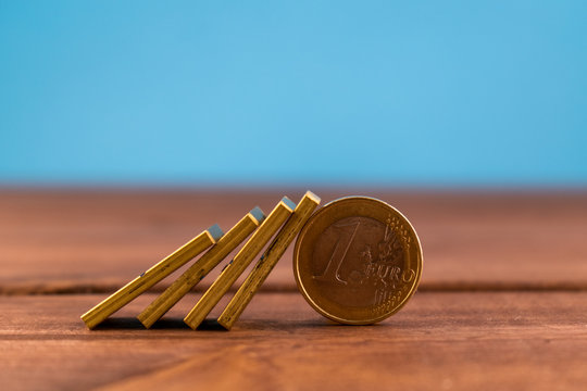One euro coin and falling golden domino on a wooden backround. Finance, crisis concept.